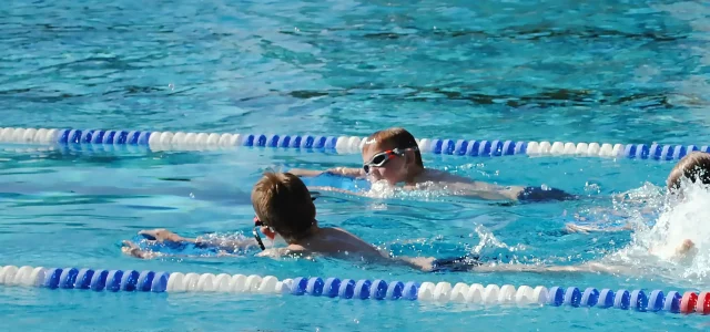 4 Kinder im Becken mit Schwimmhilfe beim Schwimmkurs
