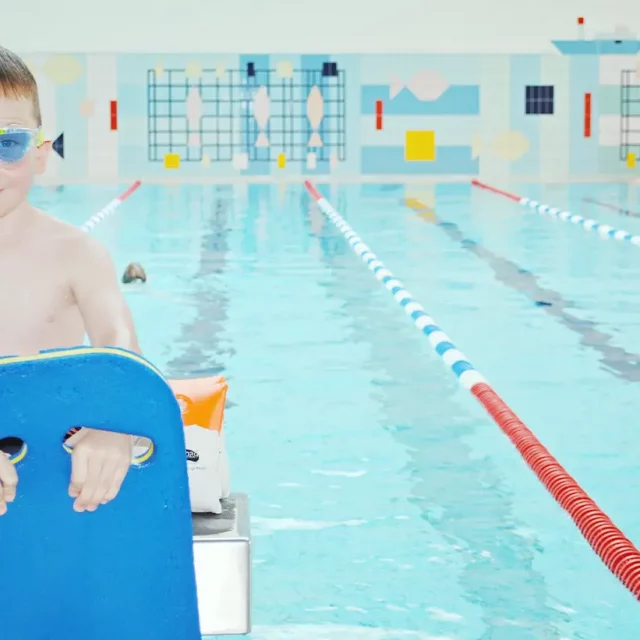 Kleiner Junge mit Taucherbrille und Schwimmhilfe in der 25-Meter-Schwimmhalle
